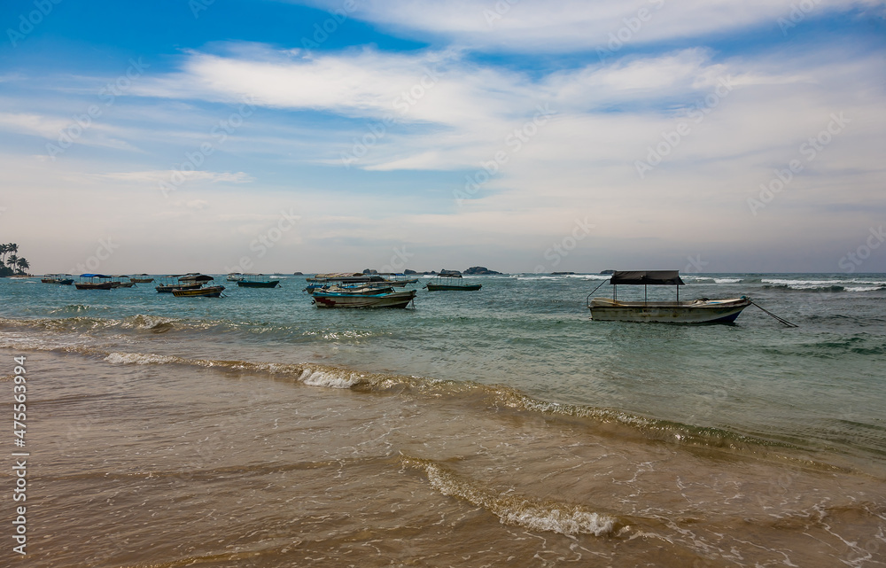 Landscape with a sandy seashore with boats against the sky with clouds in the city of Hikkaduwa in Sri Lanka