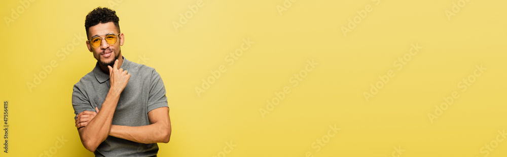 pensive african american man in sunglasses isolated on yellow, banner. pensive african american man in sunglasses isolated on yellow, banner.
