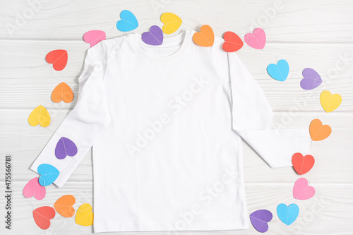 Mockup kids white t shirt with paper colorful hearts. Happy Valentines Day baby apparel flatlay on white wood background, flat lay, top view, copy space. photo