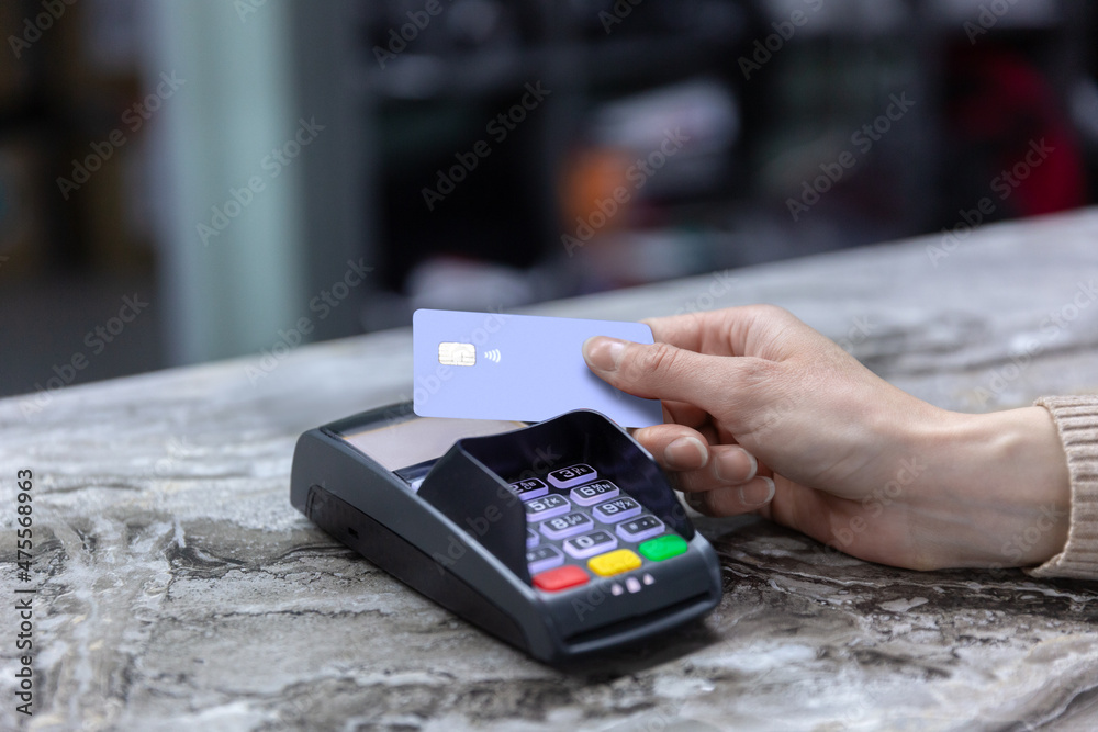 Hand of customer paying with contactless credit card with NFC technology. Bartender with a credit card reader machine at bar counter with female holding credit card. Focus on hands.