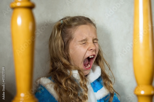 Obraz na plátně A child girl in a blue snow maiden costume yawning with her mouth wide open