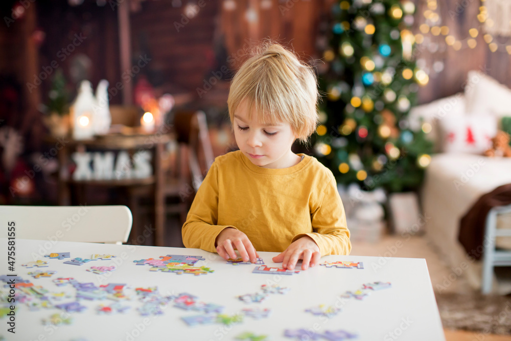 Blond child, toddler boy, having fun at home on Christmas,  assembling puzzle, enjoying