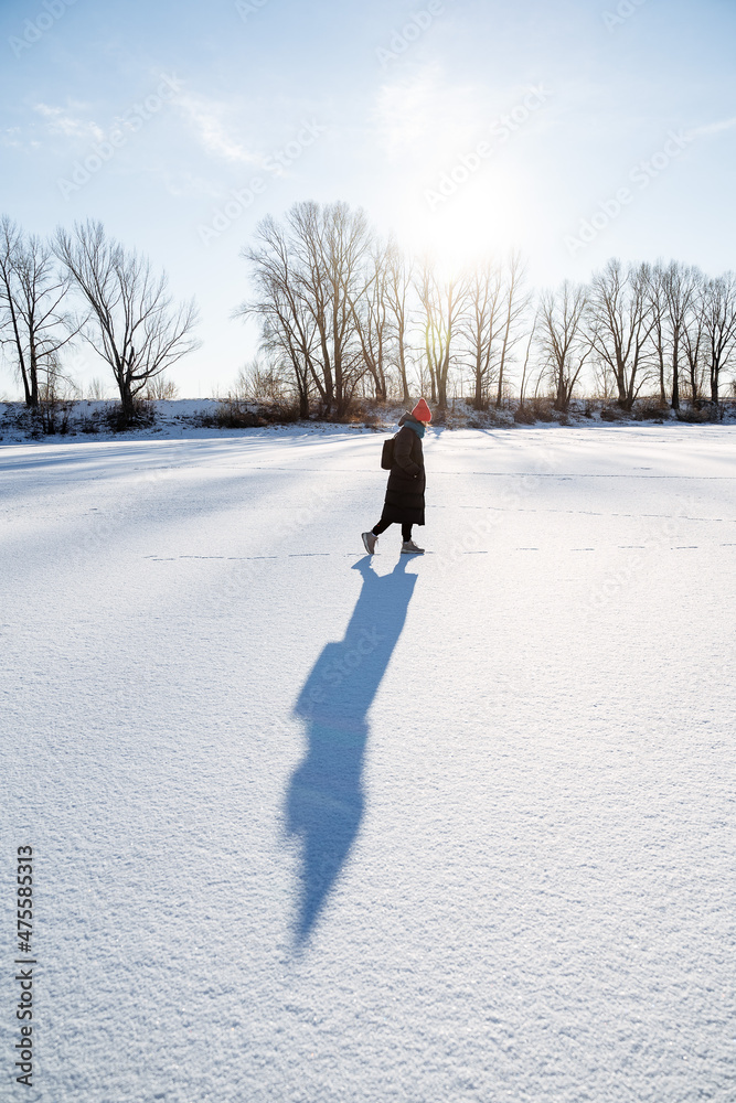 A young girl in a bright hat walks on a frozen lake. Delight and joy from the winter landscape with bright sun, clear sky. Walk in nature. A young girl in a bright hat walks on a frozen lake. Delight and joy from the winter landscape with bright sun, clear sky. Walk in nature.