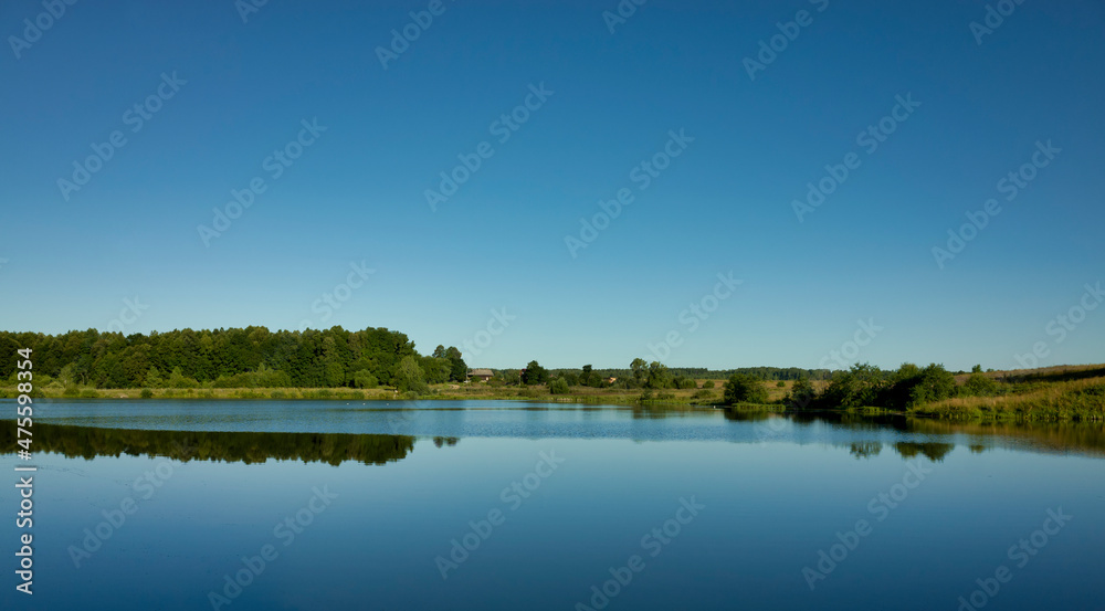 Morning lake and clear blue sky. Forest edge on the shore