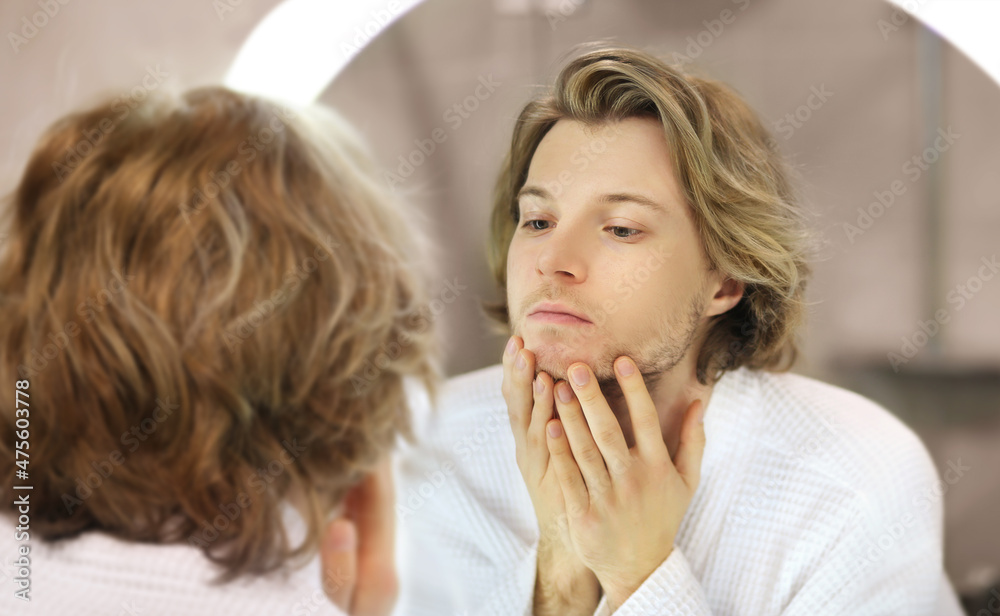 young man looking in the mirror,combing his hair,looking at problems on face young man looking in the mirror,combing his hair,looking at problems on face
