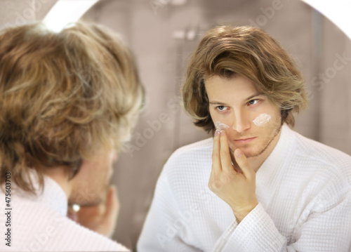 young man looking in the mirror combing his hair looking at problems on face