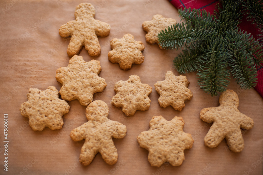 Gingerbread cookies in the form of stars and men on baking paper against the background of a spruce branch. Festive baked goods