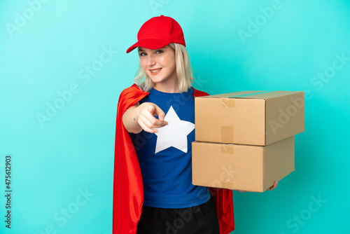 Super Hero caucasian delivery woman isolated on blue background pointing front with happy expression