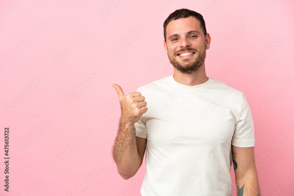 Young Brazilian man isolated on pink background pointing to the side to present a product
