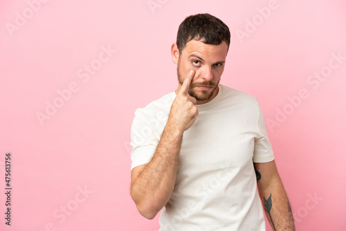 Young Brazilian man isolated on pink background showing something