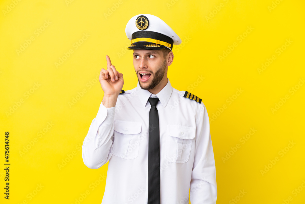 Airplane caucasian pilot isolated on yellow background intending to realizes the solution while lifting a finger up Airplane caucasian pilot isolated on yellow background intending to realizes the solution while lifting a finger up