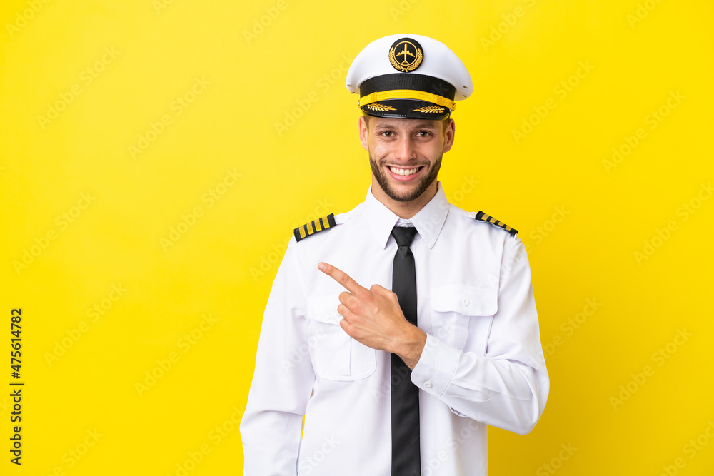 Airplane caucasian pilot isolated on yellow background pointing to the side to present a product Airplane caucasian pilot isolated on yellow background pointing to the side to present a product