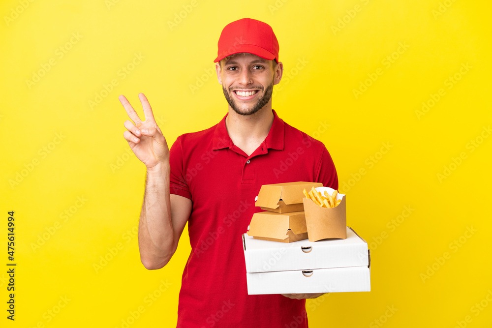 pizza delivery man picking up pizza boxes and burgers over isolated background smiling and showing victory sign pizza delivery man picking up pizza boxes and burgers over isolated background smiling and showing victory sign