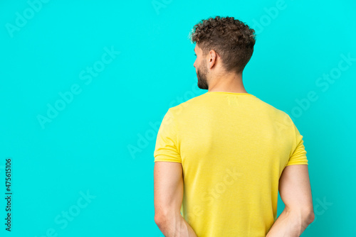 Young handsome caucasian man isolated on blue background in back position and looking back