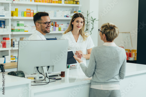 Photos Two pharmacist giving prescription medications to senior female customer in a ph