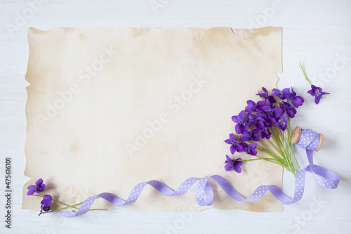 Bouquet of spring flowers of violets and a ribbon with polka dots on a white wooden background and paper for the text, congratulations.