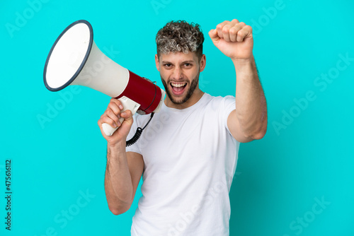 Young handsome caucasian man isolated on blue background shouting through a megaphone to announce something