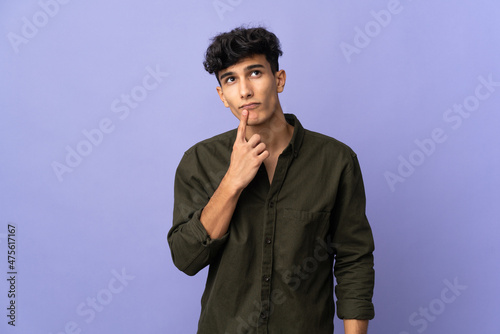 Young Argentinian man isolated on background having doubts while looking up
