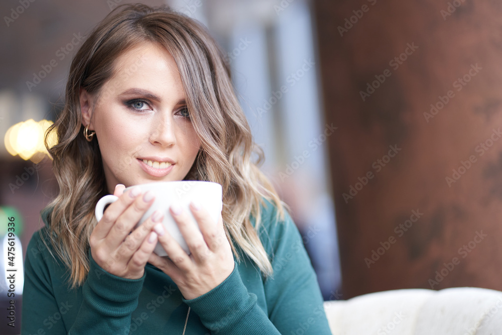 Close-up portrait of an optimistic beautiful woman with a beautiful manicure, holding a cup, sitting in a cafe, the girl looks directly into the camera. High quality photo Close-up portrait of an optimistic beautiful woman with a beautiful manicure, holding a cup, sitting in a cafe, the girl looks directly into the camera. High quality photo