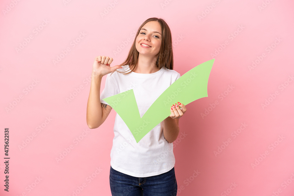 Young Lithuanian woman isolated on pink background holding a check icon with proud gesture Young Lithuanian woman isolated on pink background holding a check icon with proud gesture