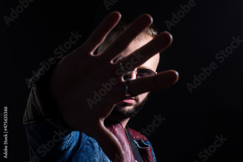 Brutal man, serious face of handsome male model, concept of men power and strong. Guy covered face with hands and doing stop gesture with sad and fear expression.