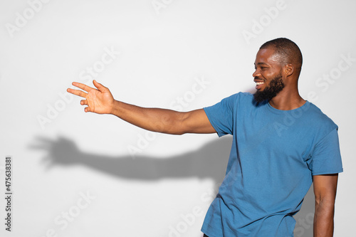 Photos Black man with a blue t-shirt smiling and showing something on a white background