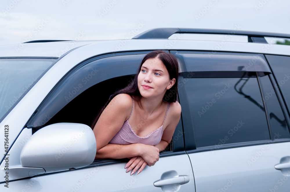 Fototapeta premium A girl with long hair leaned out of the cab of a car on the road, the concept of auto travel