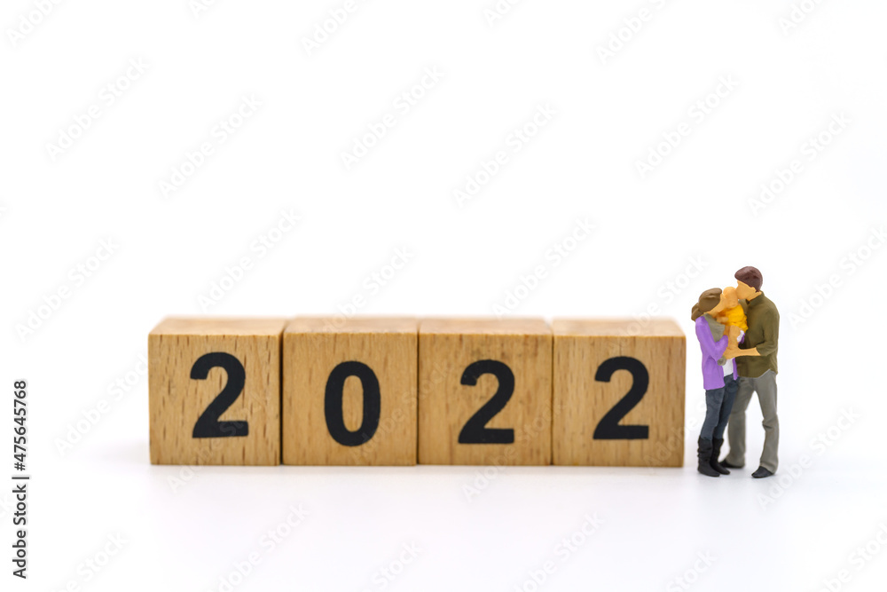 2022 New Year and Family Concept. Closeup of parent and child miniature figures hug and kissing with stack of wooden number block on white background.