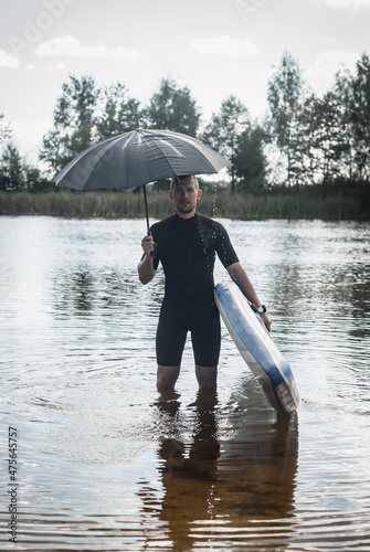 a surfer with an umbrella stands in the water, the concept of bad weather © vulkanov