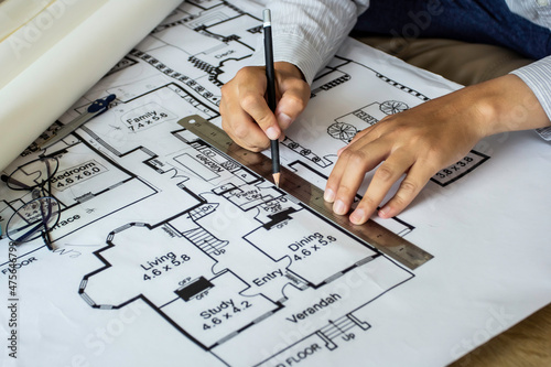 Young engineer holding a black pencil drawn with a ruler drawn to a building on a blueprint for a workplace meeting, the hand of an engineer working with tools on a background for a project drawing.