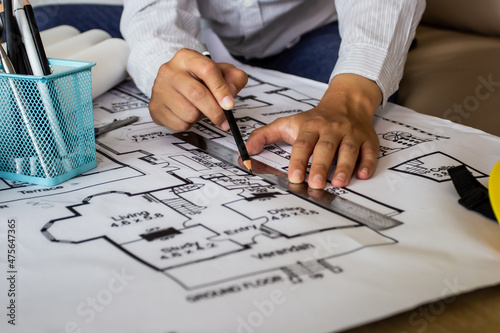 Young engineer holding a black pencil drawn with a ruler drawn to a building on a blueprint for a workplace meeting, the hand of an engineer working with tools on a background for a project drawing.