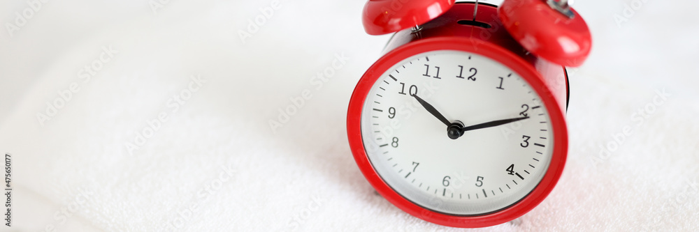 Red alarm clock stands on white towel closeup Red alarm clock stands on white towel closeup