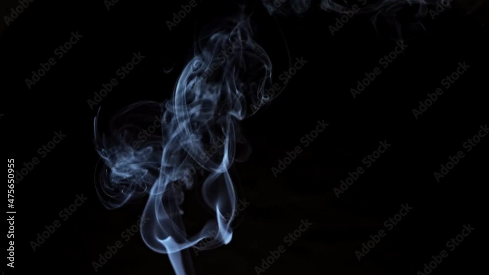 Stream of dangerous smoke rises from unextinguished aromatic candle in artificially illuminated studio room on black background closeup.