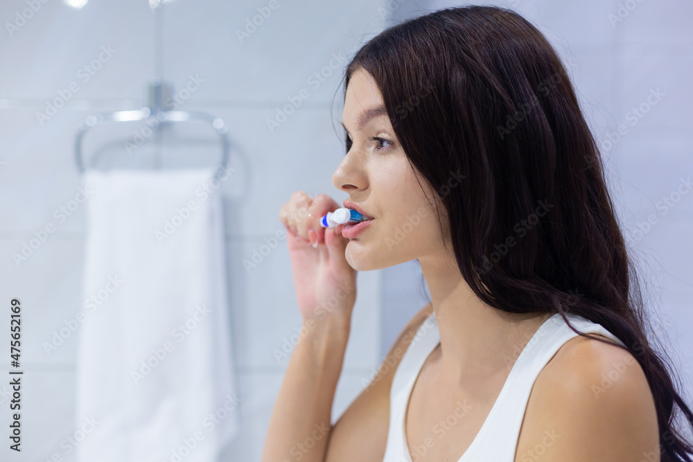 Side view portrait of pretty brunette young woman brushing her teeth in front of mirror in the morning in the bathroom Side view portrait of pretty brunette young woman brushing her teeth in front of mirror in the morning in the bathroom