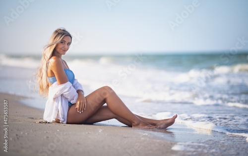 Wallpaper Mural A girl in a bluish swimsuit and shirt sits near the water edge and peers into the horizon Torontodigital.ca