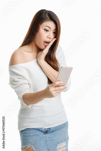 Studio shot Asian young surprised excited shocked female model in long sleeve shirt show naked shoulder standing open mouth hold hand on cheek looking at touchscreen smartphone on white background