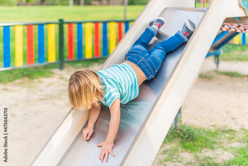 An unrecognizable little boy having fun while sliding on playground. An unrecognizable little boy having fun while sliding on playground.