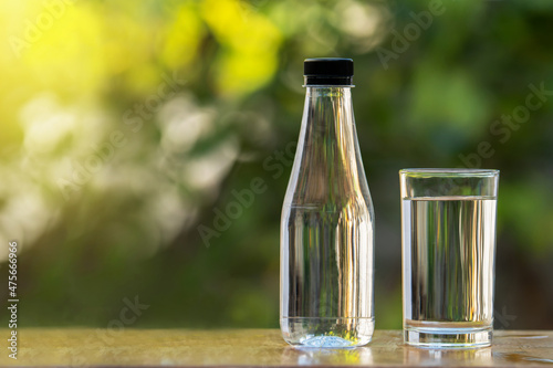 Empty glass and water bottle on wooden table on green blur background.
