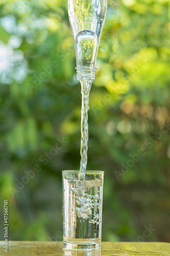 Empty glass and water bottle on wooden table on green blur background.