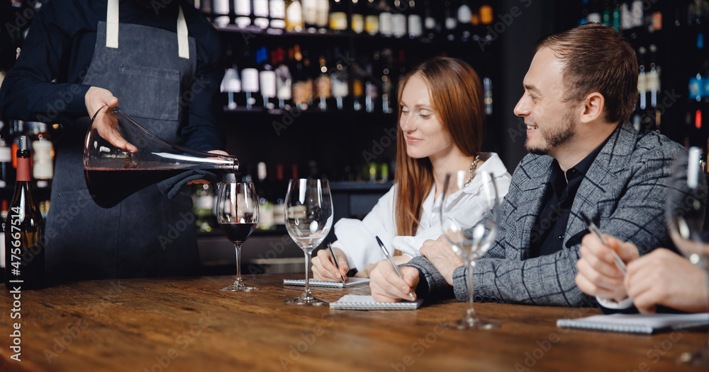 Wine degustation, young couple man and woman in restaurant tasting drinks and writing down score on blank note