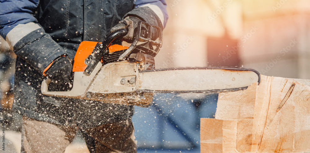 Concept construction of wooden houses. Close-up chainsaw of woodcutter sawing chain saw in motion, sawdust fly to sides