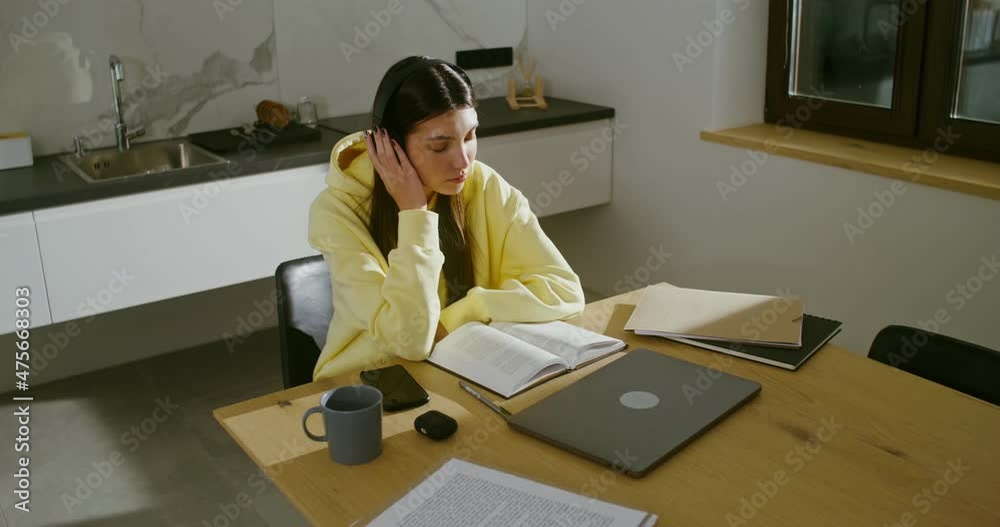 Young woman with headphones reads a book and listens to music, doing at home Young woman with headphones reads a book and listens to music, doing at home