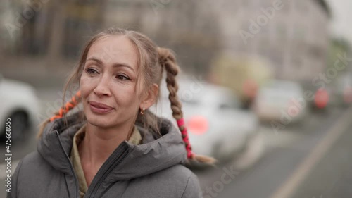 pretty middle-aged townswoman with funny hairstyle from braids is standing on street and smiling photo