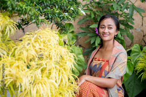 Portrait young woman with balinese face, wearing dress traditional Bali sarong in garden photo