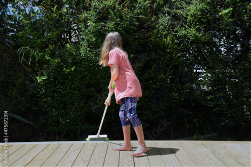 A young girl sweeps the outside deck at her house