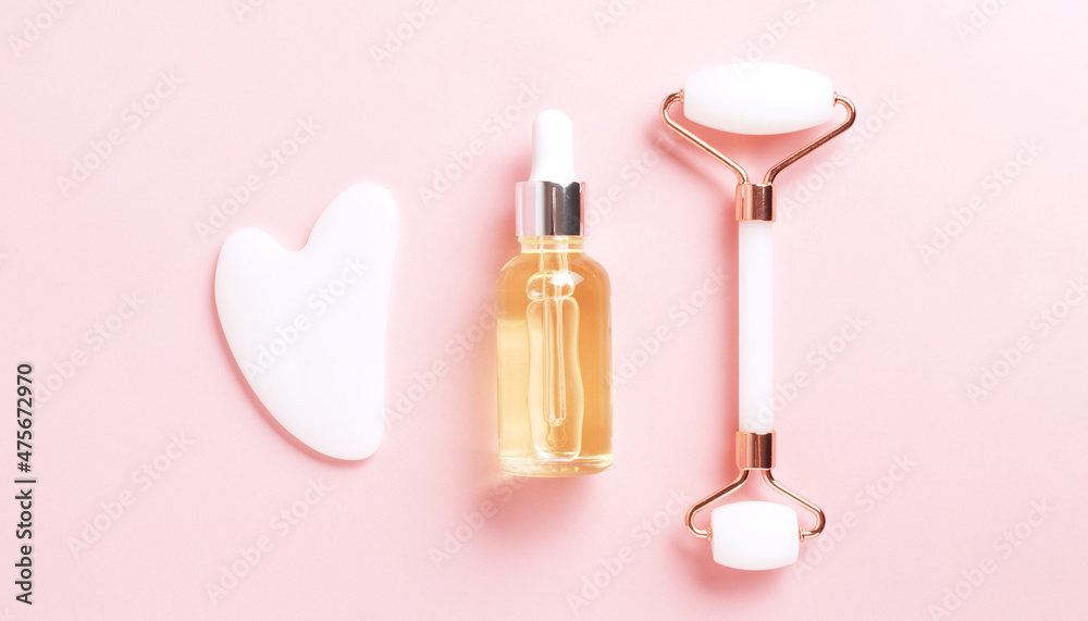 Beautiful composition of unbranded serum bottle, face roller and guasha on pink background. Creative trendy cosmetics flat lay with copy space Beautiful composition of unbranded serum bottle, face roller and guasha on pink background. Creative trendy cosmetics flat lay with copy space