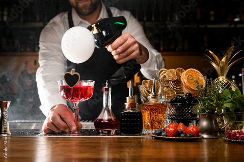 Obraz na plátne Bartender holding red tasty alcoholic cocktail and making smoke air bubble