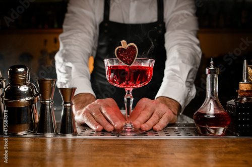 Fotografija Hands of male bartender holding glass with red alcohol cocktail