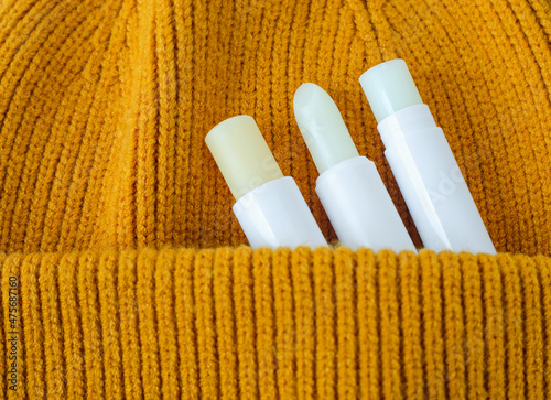 Three lip balms on an orange knitted background. Winter lip care sticks with beeswax, honey, panthenol and shea butter. Copy space. photo