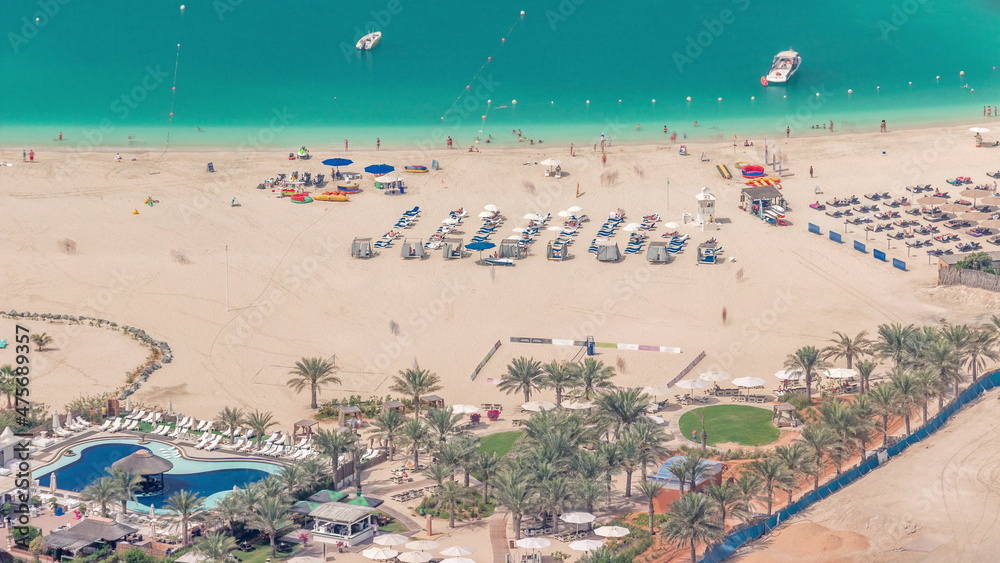 Crowded JBR beach with tourists enjoying the sun and the sea, sitting under umbrellas aerial top view from above timelapse